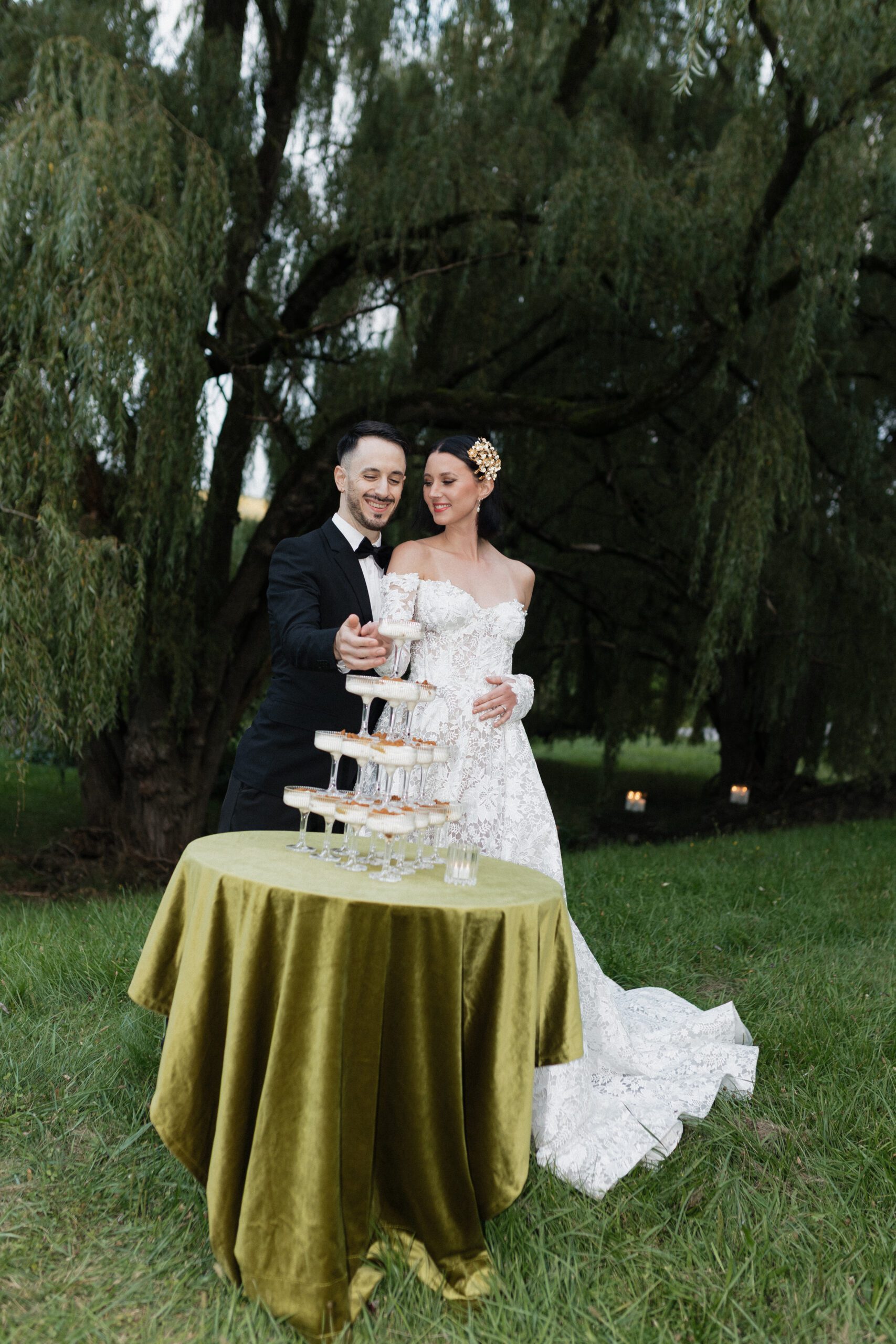 Bride and groom standing before a champagne tower beneath a willow tree at a Finger Lakes wedding venue, photographed by Valerie Marie Photography.