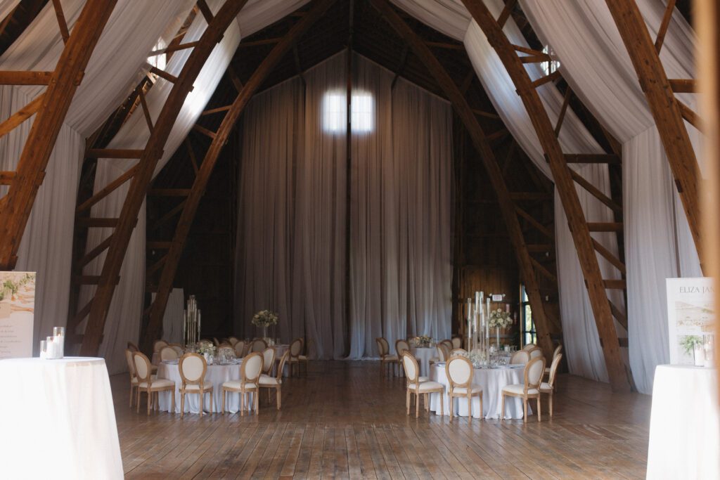 Elegant barn reception space at The Wells Estate in Avon, New York, featuring tall ceilings, soft candlelight, and refined decor